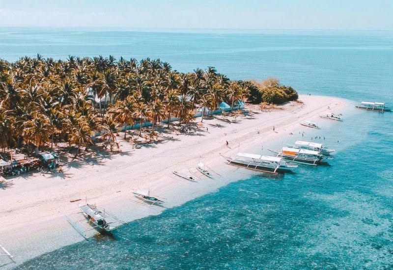 Aerial view of Islas Moriones Beach Resort's beach on Maniwaya Island, Marinduque, with outrigger boats and coconut palms along the shore